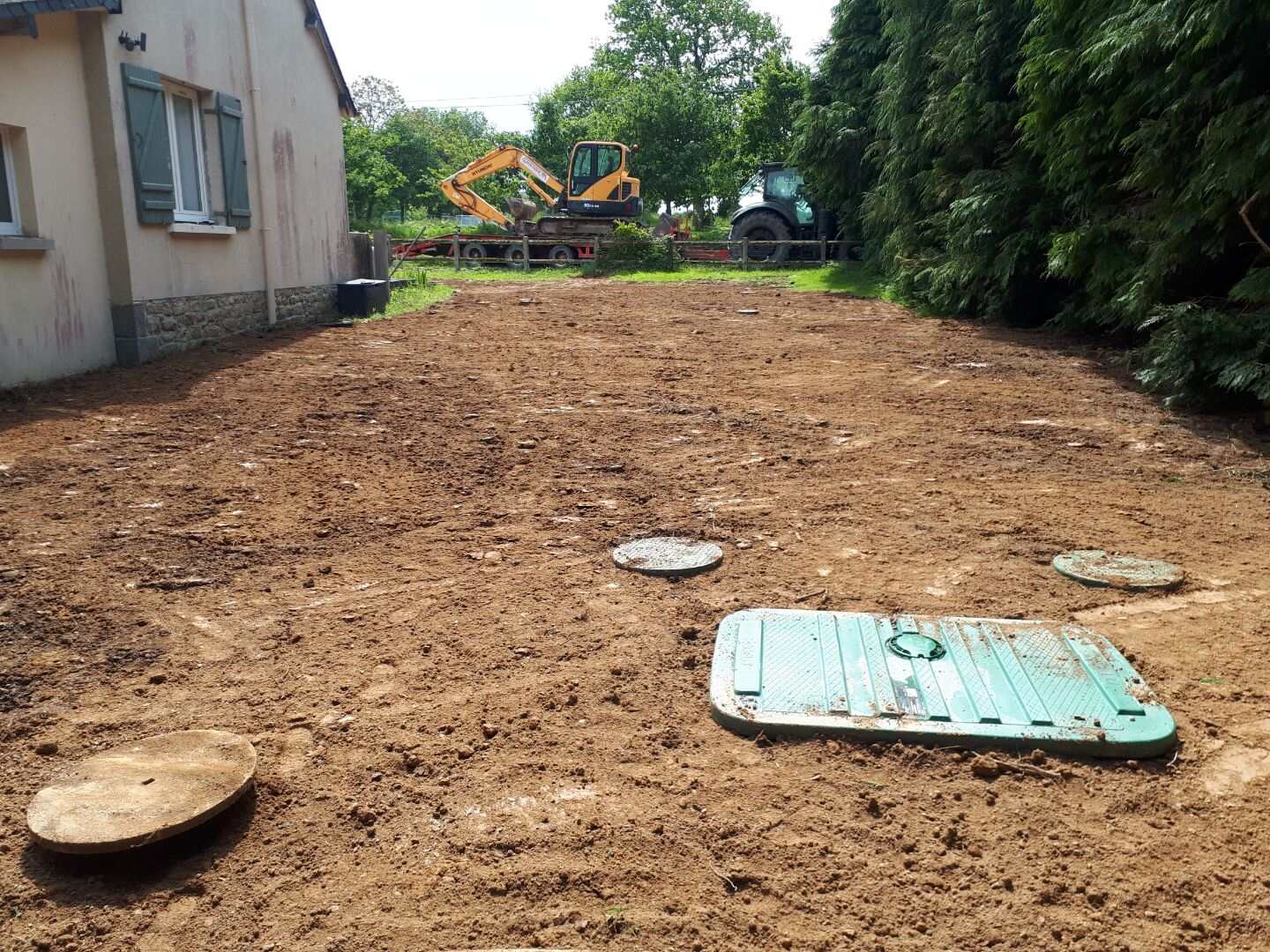 Terrain nivelé en fin de chantier d'assainissement, pelle mécanique et tracteur en arrière-plan