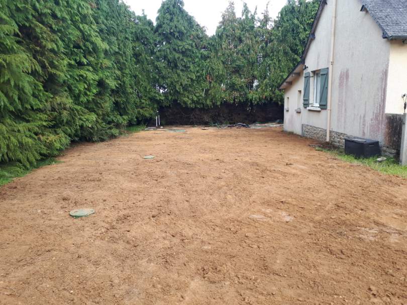Terrain nivelé après pose d'assainissement, regards visibles entre la maison et une haie