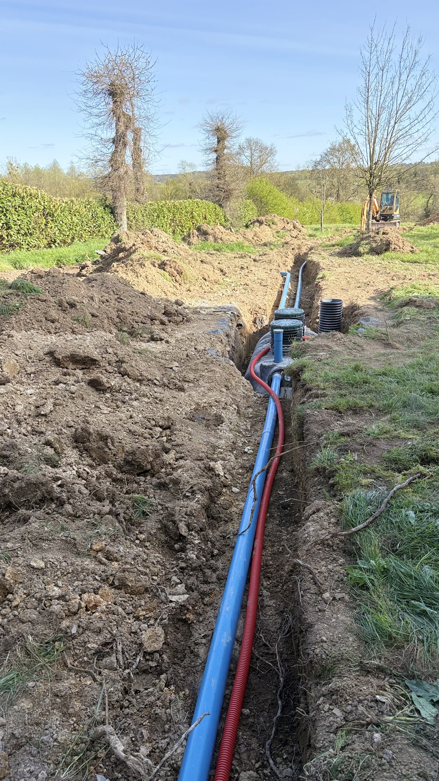 Tranchée de relevage des eaux avec chambre de pompage, canalisation bleue et gaine électrique rouge